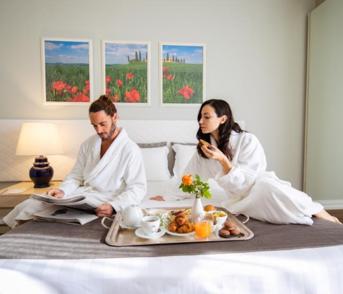 Couple in bathrobes having breakfast in bed with a newspaper.