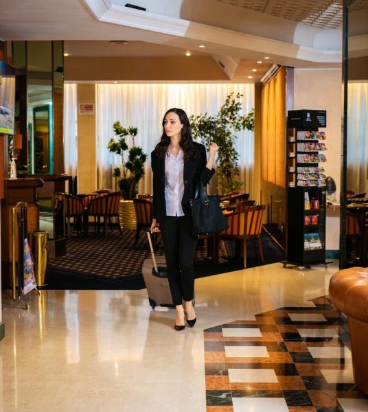 Donna con valigia entra in un hotel elegante, arredamento moderno e accogliente.