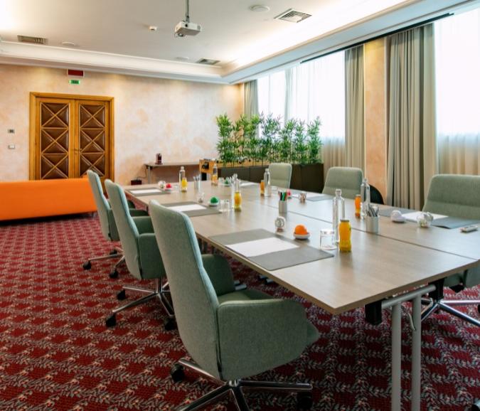 Sala riunioni con tavolo, sedie verdi, bevande e decorazioni verdi.