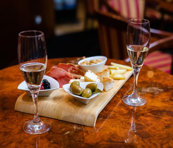 Tagliere con salumi, formaggi, olive e due calici di vino su tavolo.
