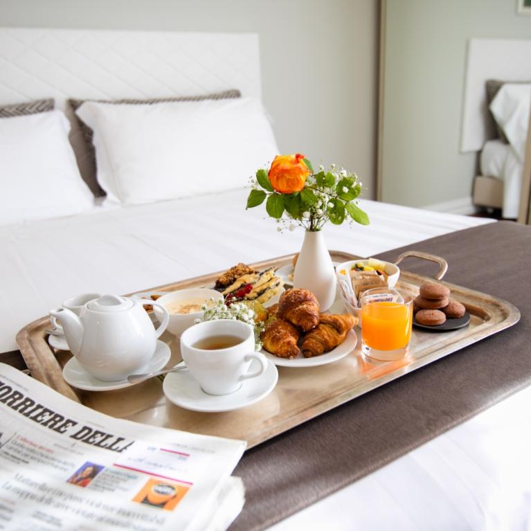 Colazione a letto con tè, croissant, succo e giornale su un vassoio elegante.