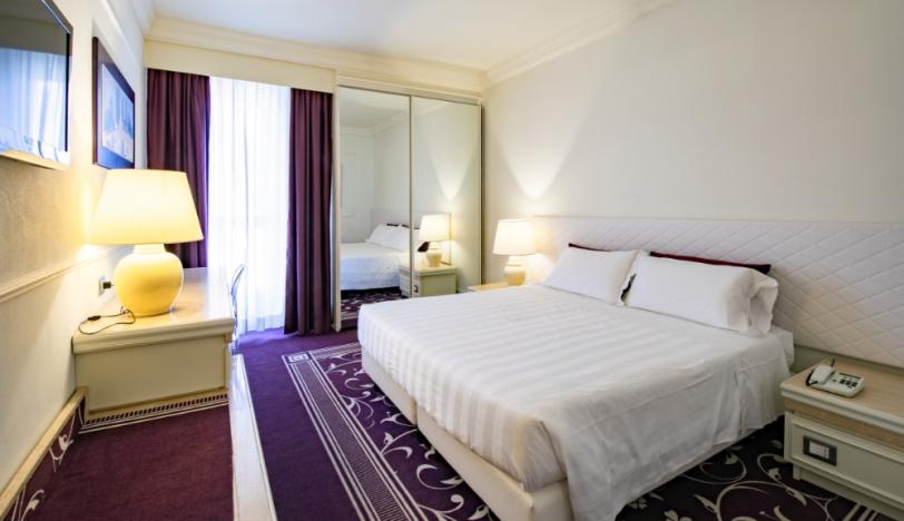Camera d'albergo elegante con letto matrimoniale, specchio grande e arredamento moderno.