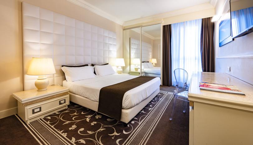 Camera elegante con letto matrimoniale, specchio, TV e arredi moderni.