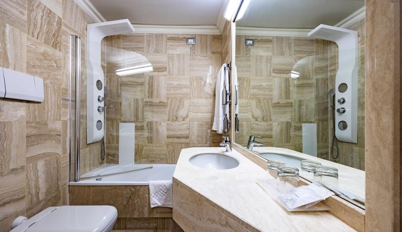 Bagno moderno con pareti in marmo, doccia, lavabo e specchio ampio.