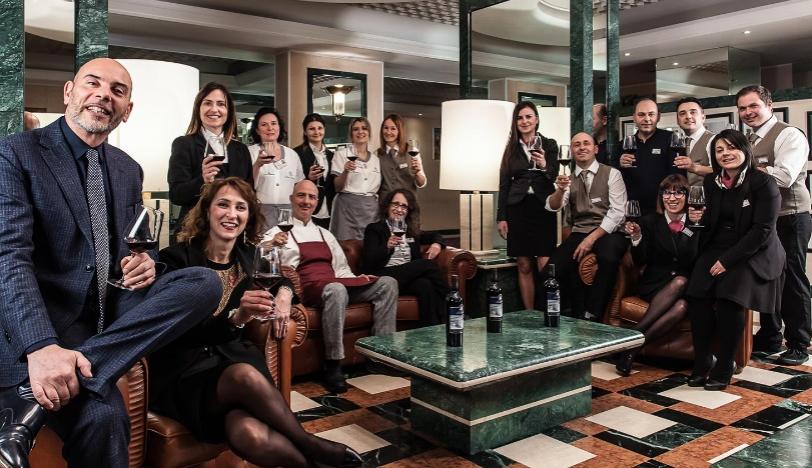 Gruppo di persone eleganti con bicchieri di vino in un ambiente lussuoso.