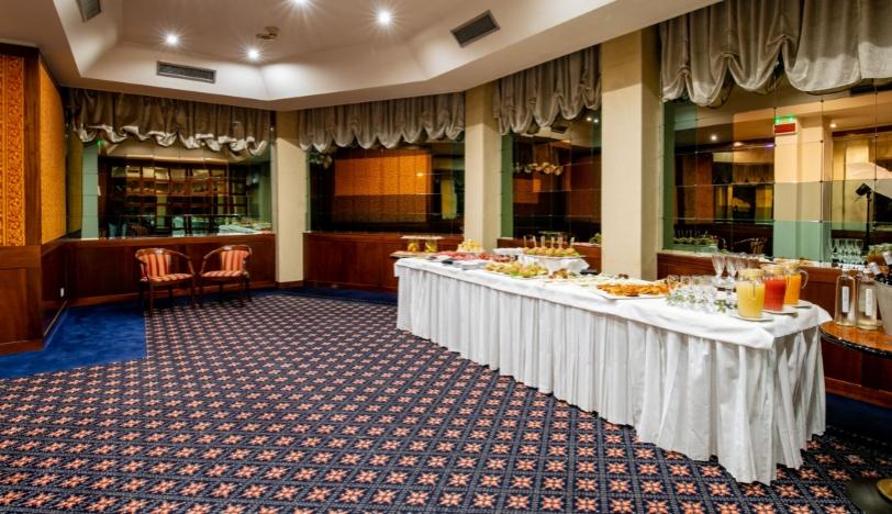 Sala con buffet, tavolo imbandito, moquette decorata e illuminazione soffusa.