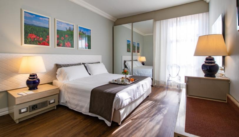 Camera elegante con letto matrimoniale, lampade, specchio e decorazioni floreali alle pareti.