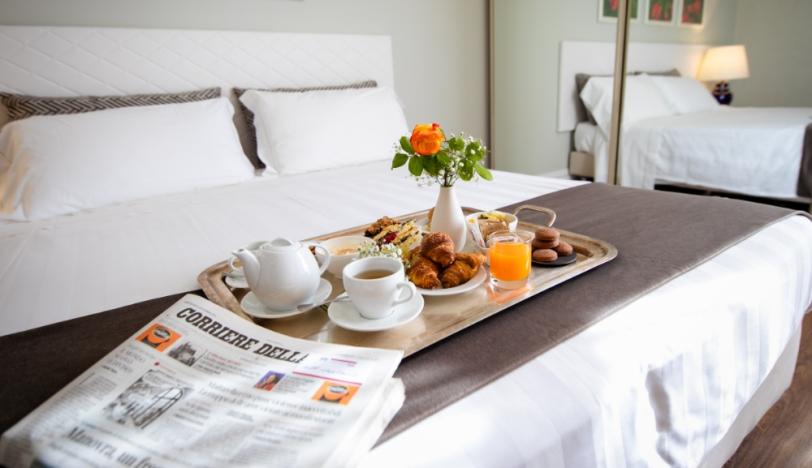 Colazione a letto con giornale, fiori e dolci su un vassoio elegante.
