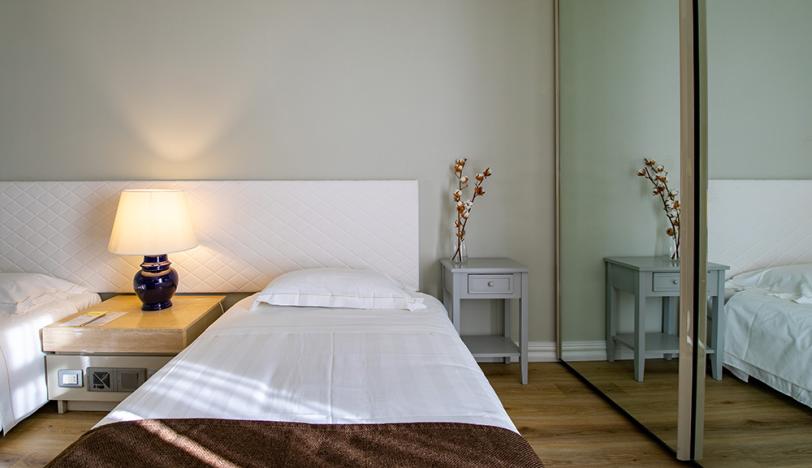 Camera da letto moderna con letto singolo, lampada, specchio e comodino grigio.