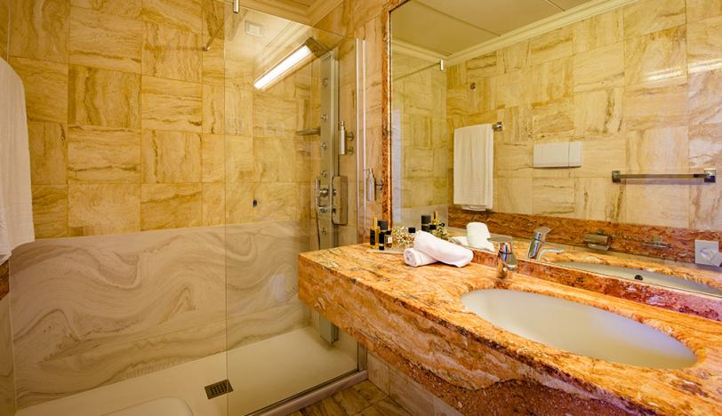 Bagno elegante con doccia in vetro, lavabo in marmo e ampio specchio.