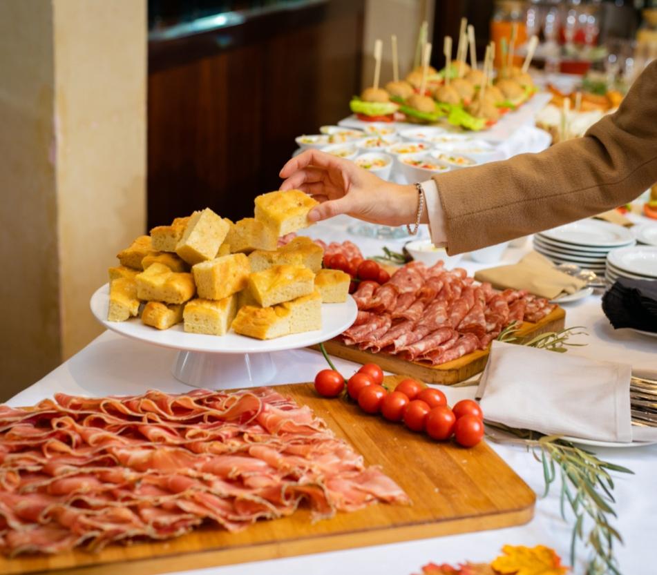 Buffet con focaccia, affettati e pomodorini su un tavolo imbandito.